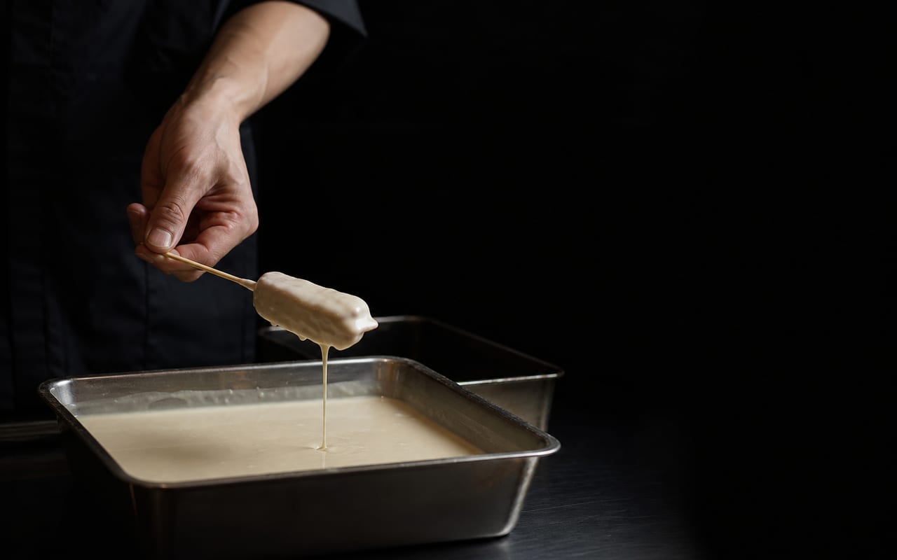 バッター液に串をくぐらせる料理人の手元